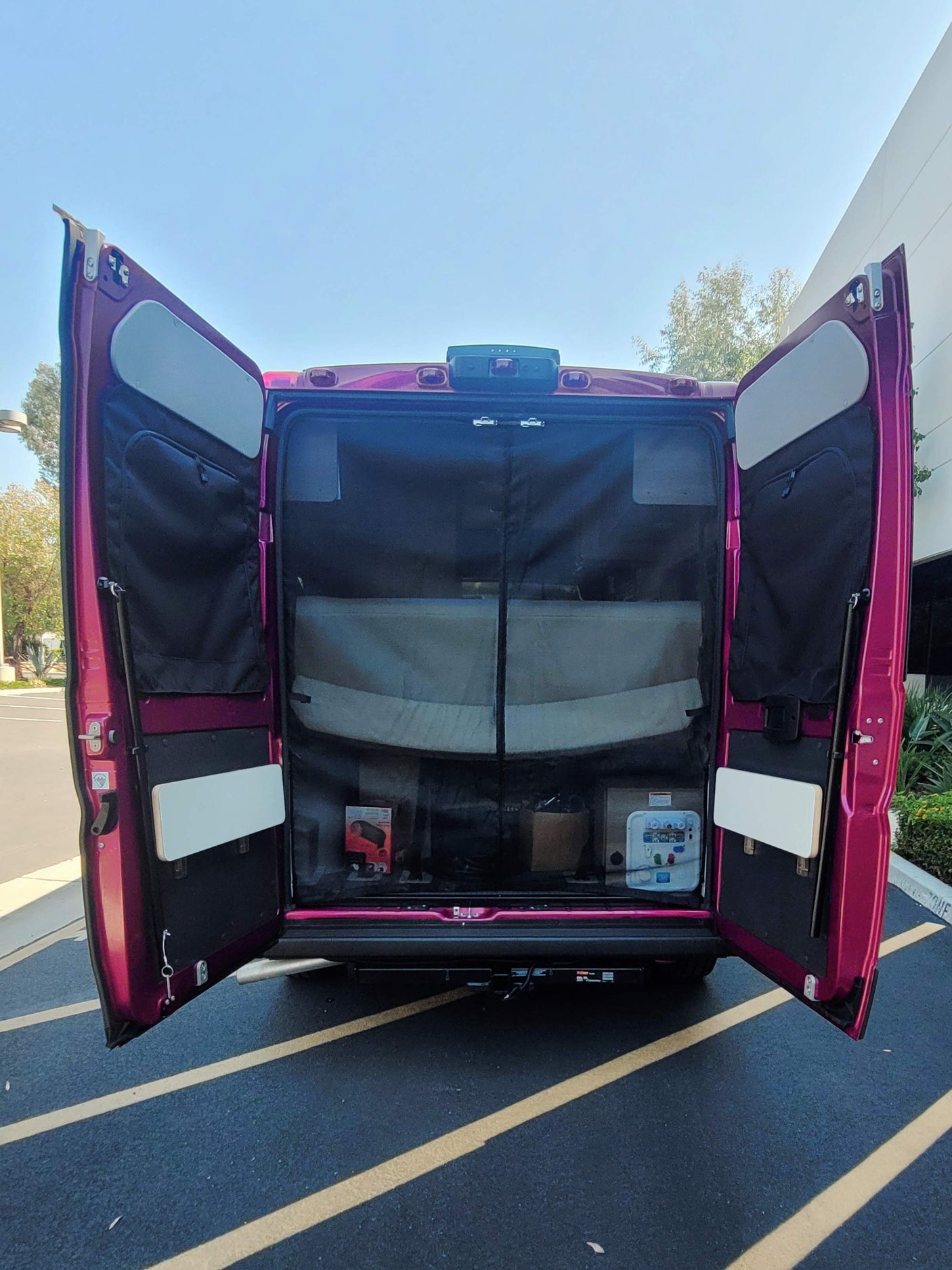 Open rear doors of a purple RV rental show a functional interior with storage pockets, a table, and mesh screen.
