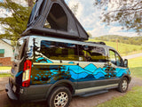 A custom camper van with a mountain/forest wrap & open rooftop tent, perfect for an RV rental in scenic outdoors.