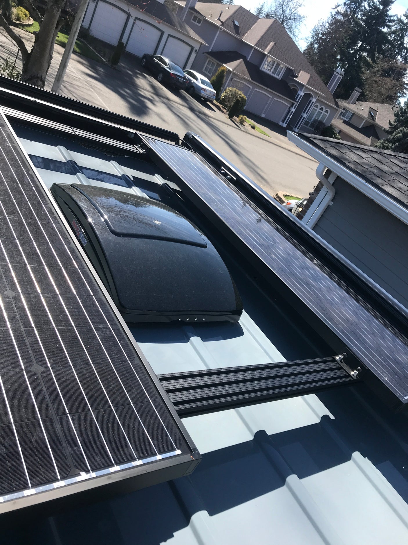 RV rental roof, featuring solar panels and a MaxxAir vent, parked on a residential street with houses in the background.