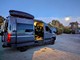 A grey Sprinter van RV rental, side door open and interior lit, parked under evening moonlight. Ideal for camping and van life.