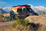 This vibrant custom RV rental is perfectly parked for camping, offering stunning views of snowy mountains and desert flora.