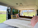Cozy camper van RV rental interior with a comfy bed, kitchenette, and scenic nature views.