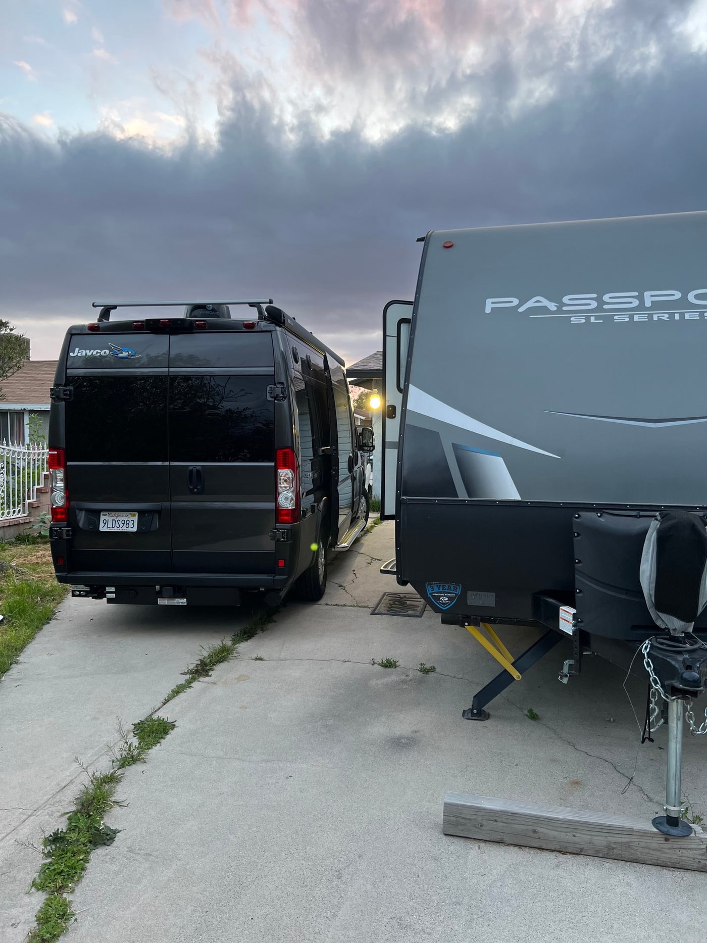 An rv rental setup: dark camper van and Passport travel trailer parked on a driveway under an overcast sky. — photo 10