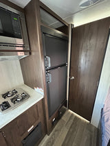 RV rental interior: kitchen with microwave, cooktop, and built-in fridge. Dark wood cabinetry & flooring complement a closed door.