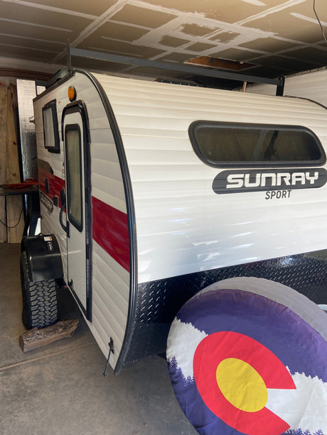 White & red Sunray Sport travel trailer/camper, ideal for RV rental. Features a Colorado spare tire cover.