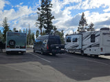 Three RVs, including a Cruise America rv rental and a Jayco Greyhawk, are parked outdoors amidst pine trees under a cloudy sky.
