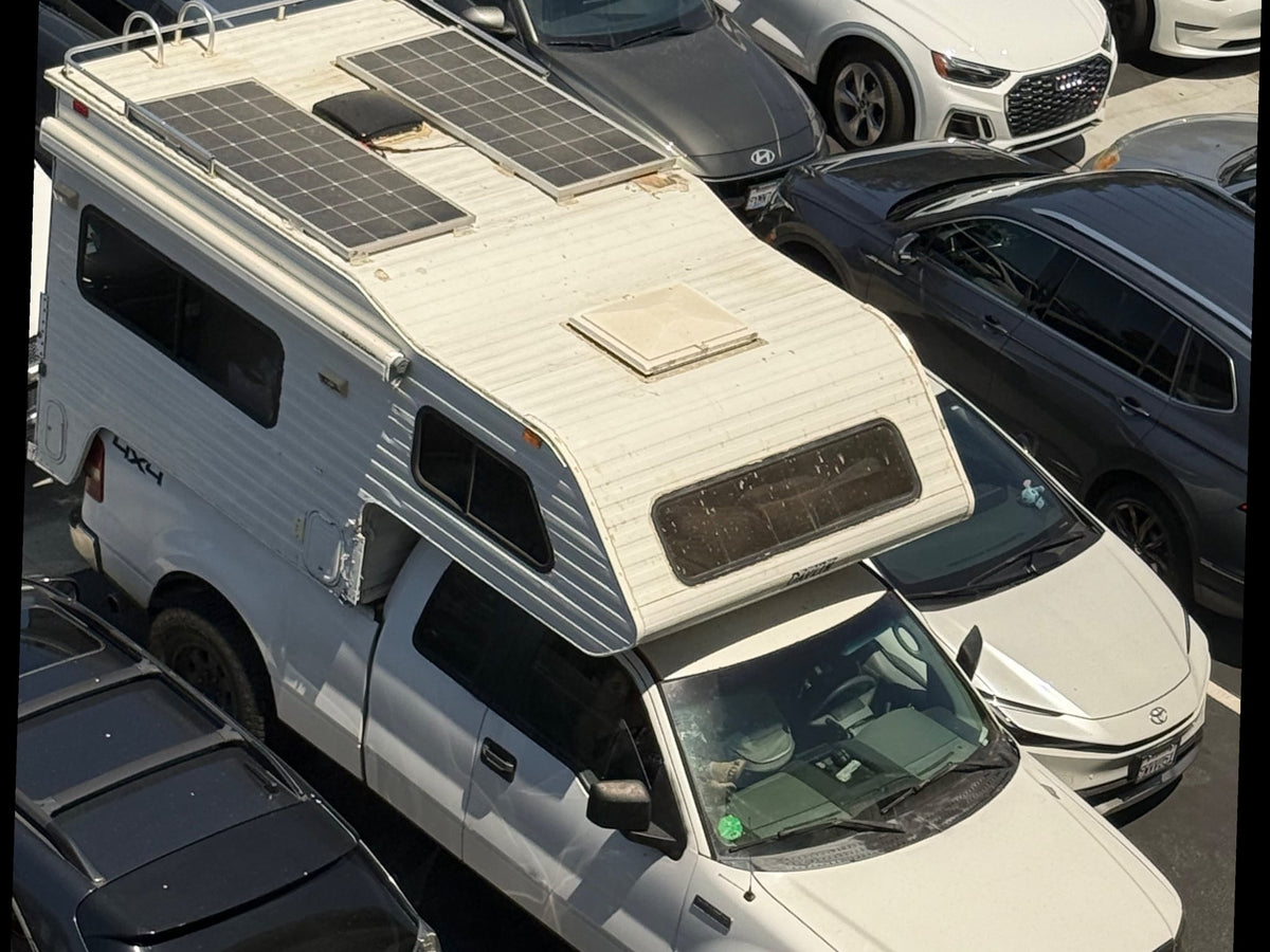 is parked off-road before snowy mountains at sunset.|A white Ford F-150 pickup truck with a large white RV rental truck camper attached — photo 3