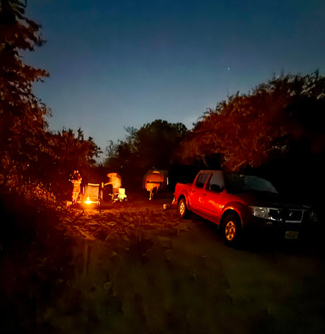 Enjoying a serene night outdoors with an RV rental, a warm campfire, and a truck under a crescent moon.