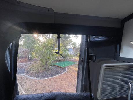 View from an RV rental's screened window shows a sunny backyard with trees and a sandy path.