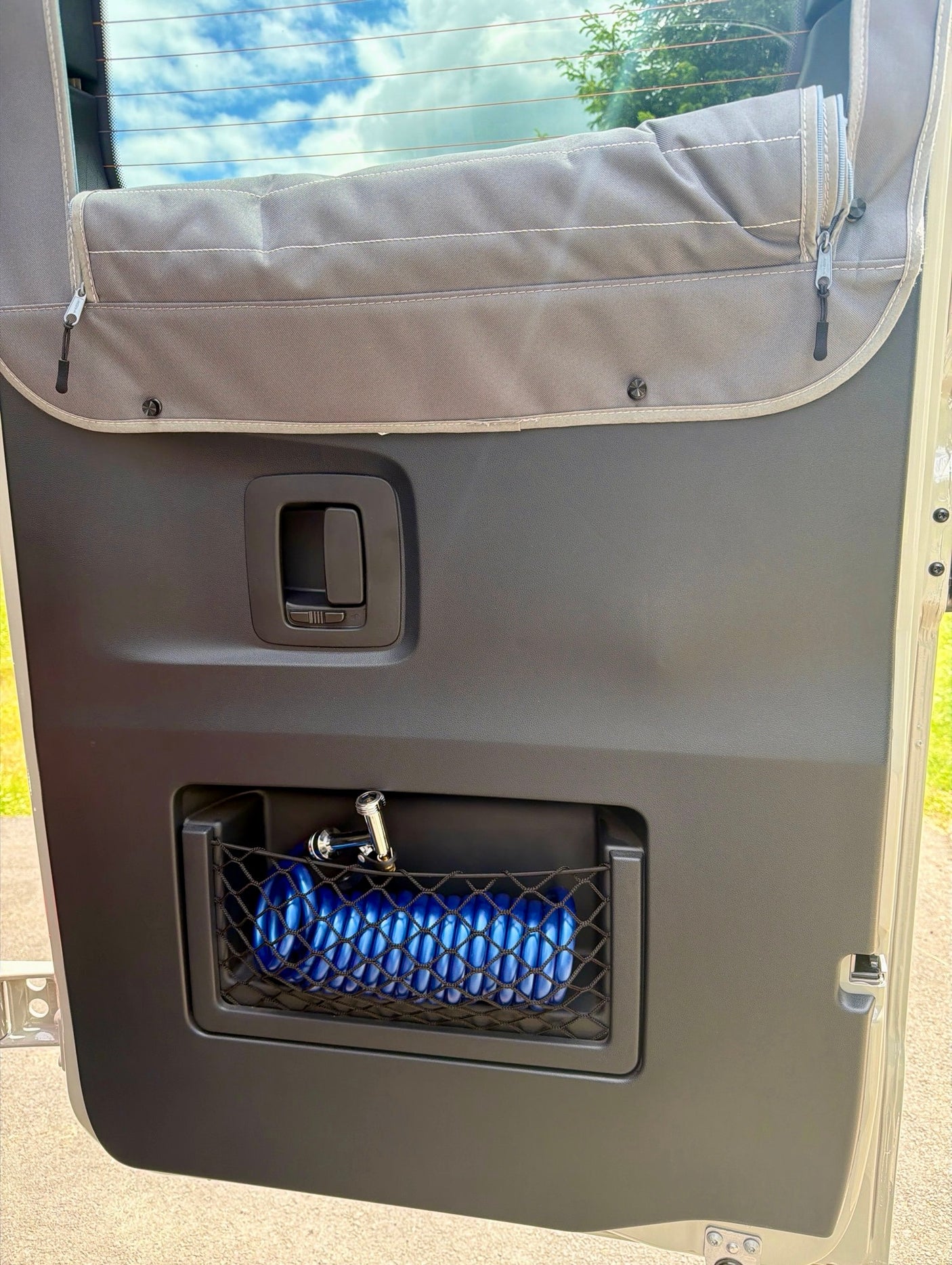 RV rental interior: Organized door panel features a mesh storage net with a blue hose, and a fabric window cover.