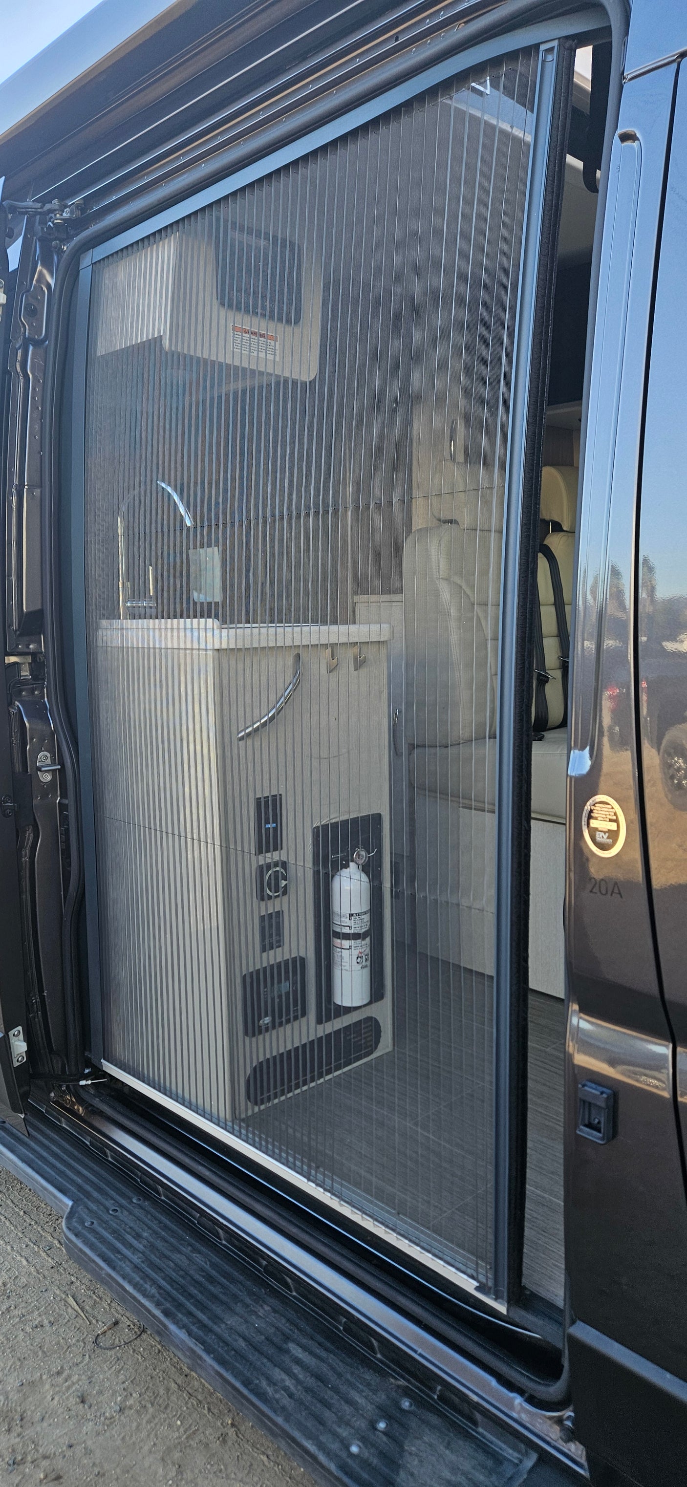 A pulled-across mesh screen door on an **RV rental** reveals its interior, including a galley counter, controls, and seating.
