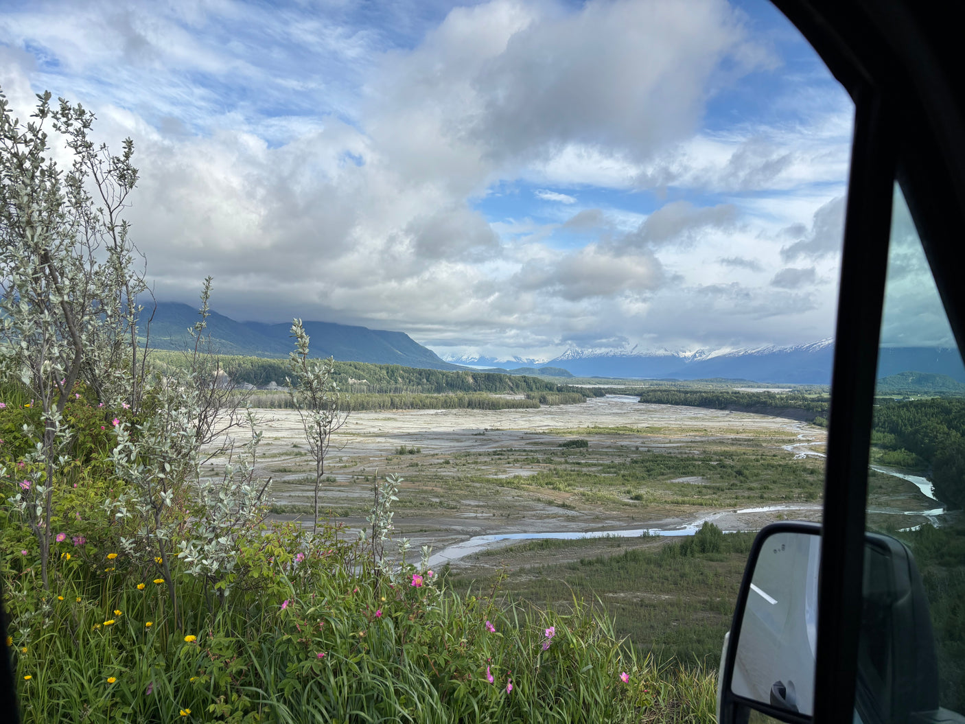 Stunning view from an RV rental overlooking a braided river, lush valley, and distant snow-capped mountains in Alaska.