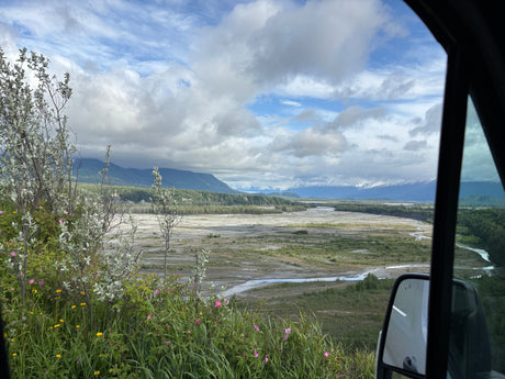 Stunning view from an RV rental overlooking a braided river, lush valley, and distant snow-capped mountains in Alaska.