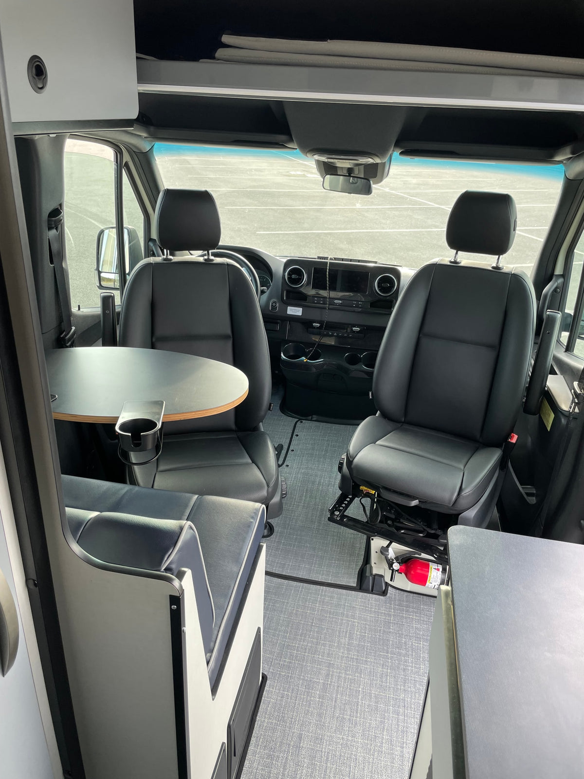 Spacious RV rental van interior with swiveling front seats, dinette table, and overhead storage. Fire extinguisher by passenger. — photo 7