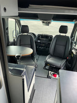 Spacious RV rental van interior with swiveling front seats, dinette table, and overhead storage. Fire extinguisher by passenger.