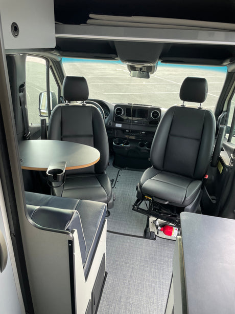 Spacious RV rental van interior with swiveling front seats, dinette table, and overhead storage. Fire extinguisher by passenger.