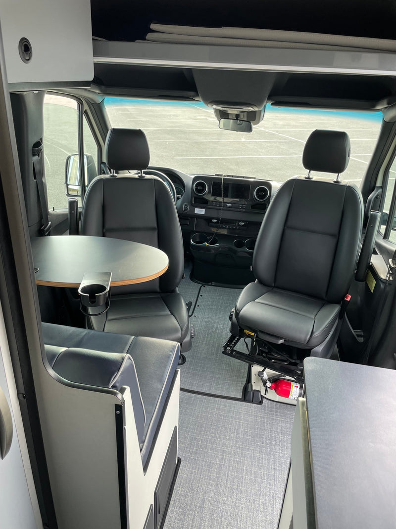 Spacious RV rental van interior with swiveling front seats, dinette table, and overhead storage. Fire extinguisher by passenger. — photo 7