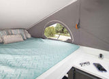 Inside this RV rental: a cozy bed with pillows, a scenic window view, and a convenient bedside counter with essentials.