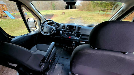 RV rental's front cabin: steering wheel, dash, and outside yard with playset visible through windshield.