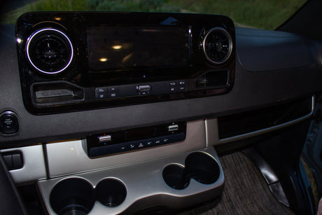 Dashboard of an **RV rental**, featuring an infotainment screen, circular air vents, climate controls, and cup holders.