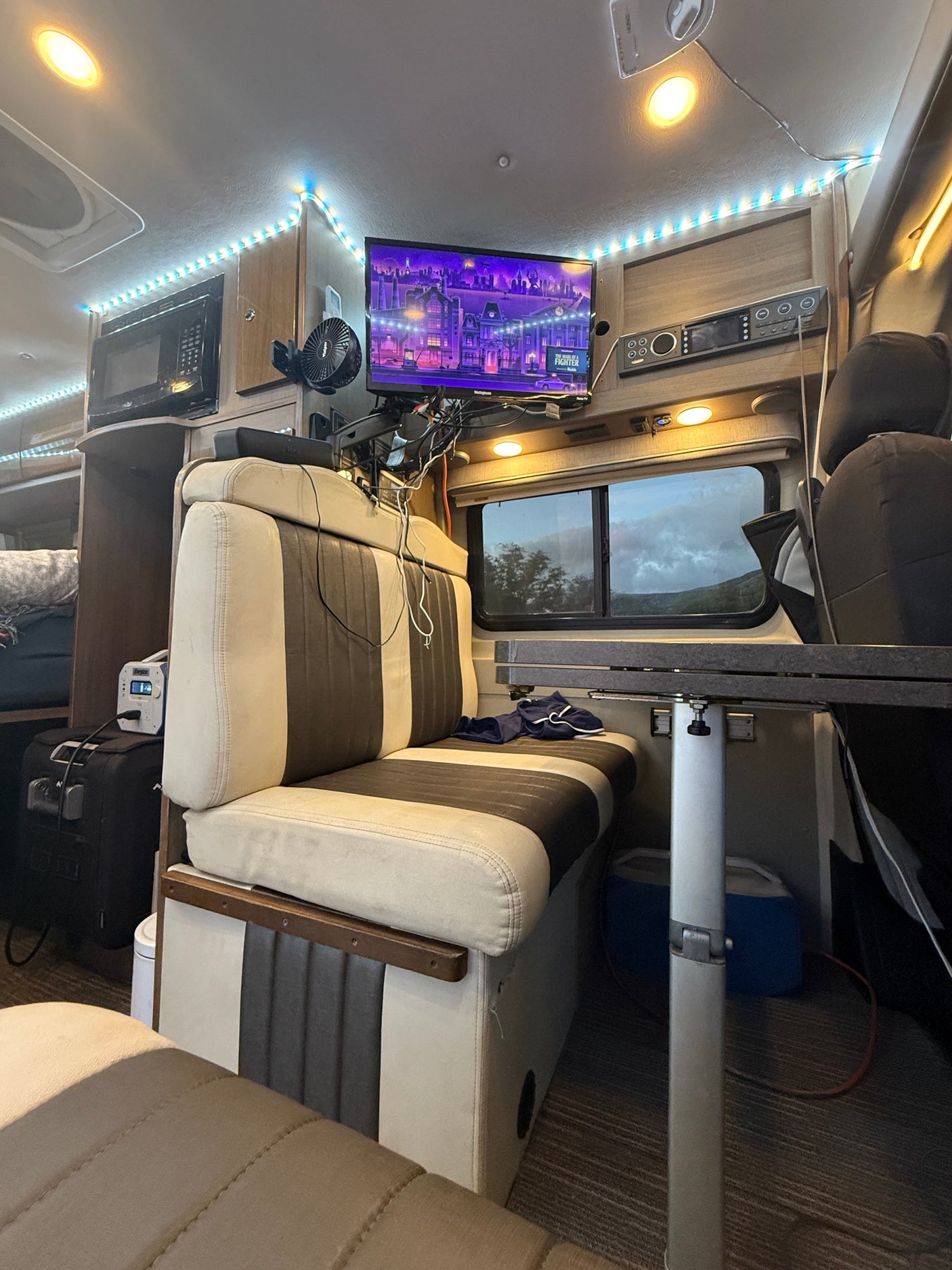 Brightly lit RV rental dinette with TV, microwave, and scenic window view for comfortable journeys.