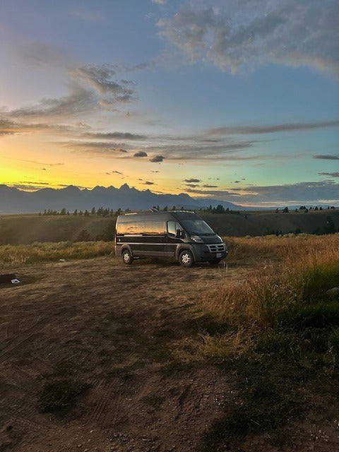 An RV rental camper van parked before majestic mountains as a vibrant sunset paints the sky. Ideal for nature exploration.