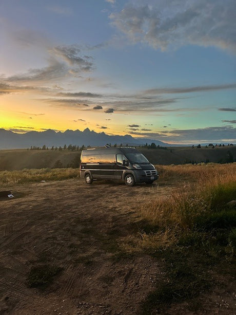 An RV rental camper van parked before majestic mountains as a vibrant sunset paints the sky. Ideal for nature exploration.