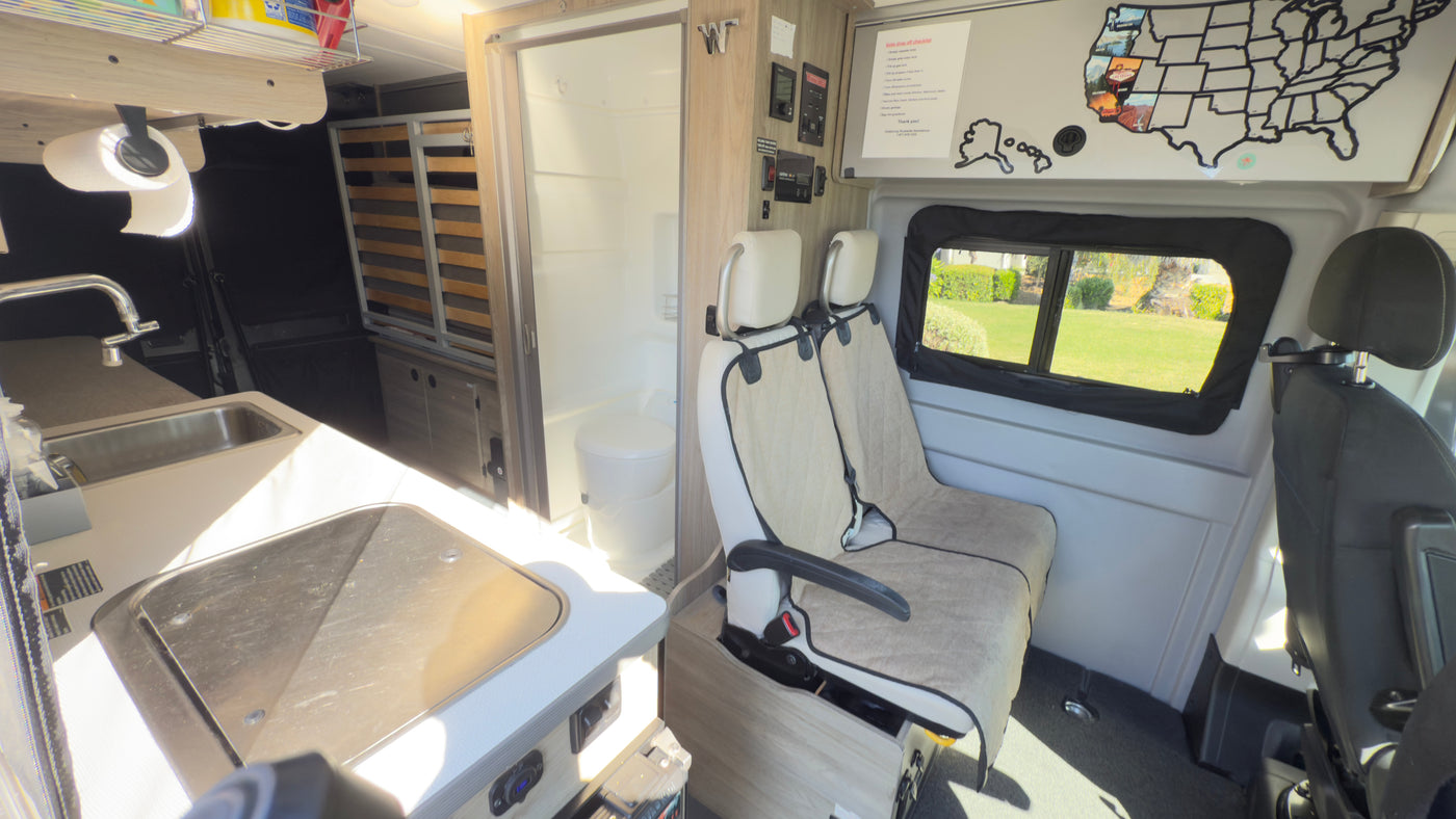 View inside an RV rental: kitchenette with sink/stove, compact bath, and passenger seating, ready for road trips. — photo 13