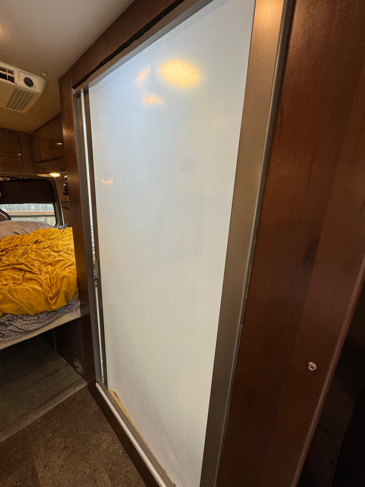 RV rental interior: a frosted sliding door next to dark wood cabinetry, revealing a bedroom with a bed and overhead AC unit.