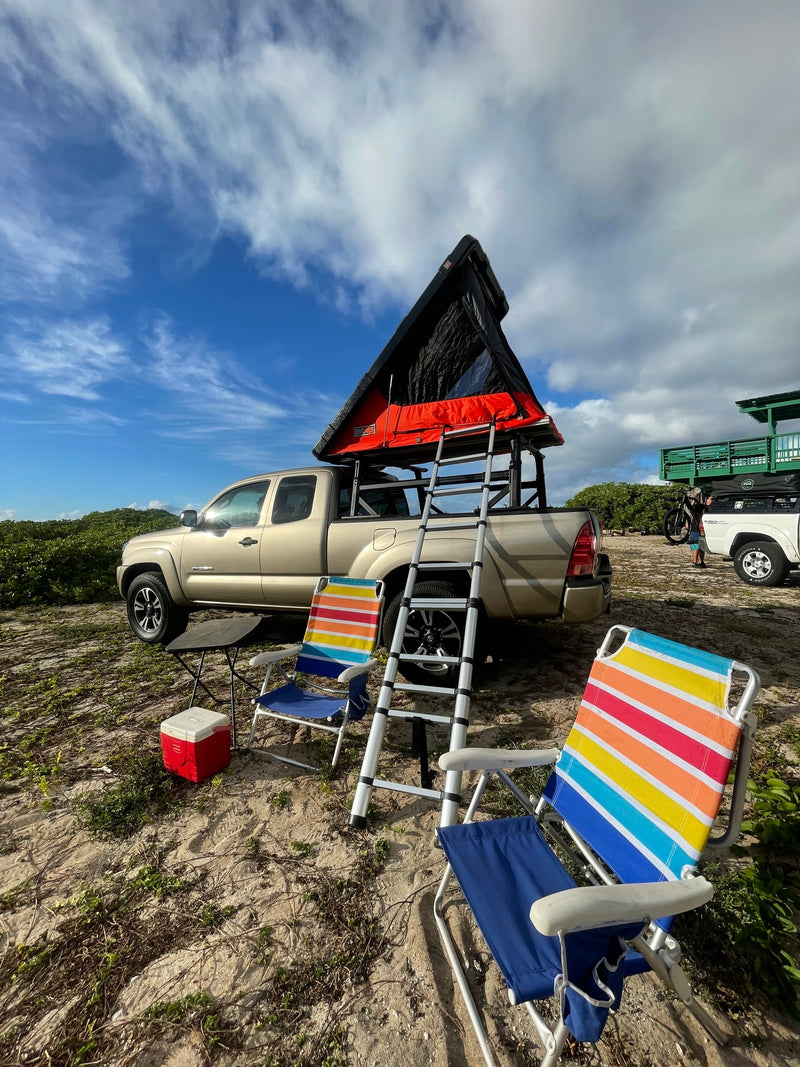 Scenic beach camp setup! Tan truck with a rooftop tent, ladder, and colorful chairs. Consider an rv rental for adventure. — photo 9