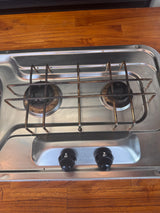 Stainless steel two-burner gas stove with 'OFF' knobs set in a wooden counter, typical for an RV rental kitchen.
