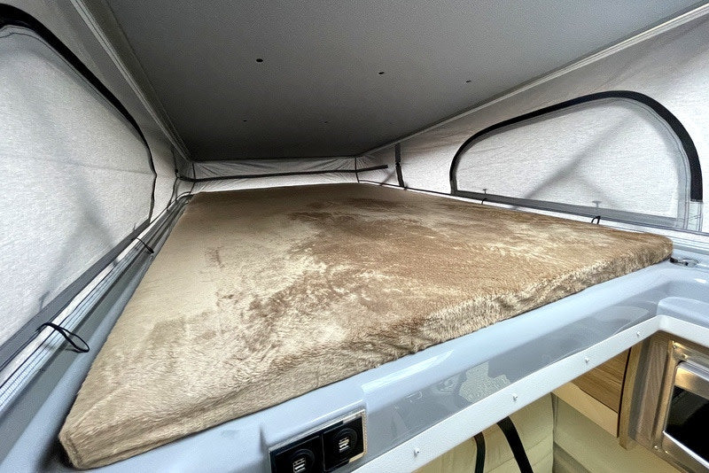 Inside an RV rental: a plush pop-top bed with mesh windows. Perfect camper sleeping area for comfortable travel adventures.