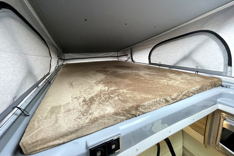 Inside an RV rental: a plush pop-top bed with mesh windows. Perfect camper sleeping area for comfortable travel adventures.