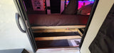 Inside an RV rental: bed lifted with gas struts to reveal spacious under-bed storage. "Don't Wake the Bear" sign on wall.