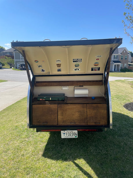 Open tailgate reveals a compact RV rental kitchen: propane stove, drawers, and paper towels ready for camping!