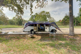 Explore the open road with an RV rental! This white campervan shows its camping setup with an extended awning by a park.