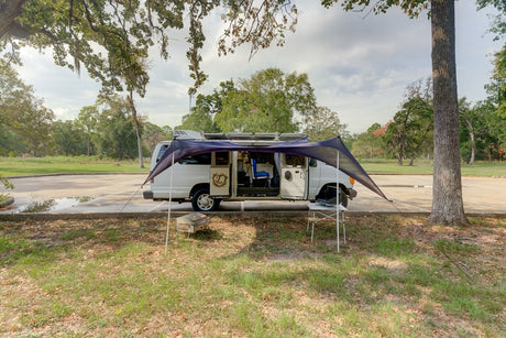 Explore the open road with an RV rental! This white campervan shows its camping setup with an extended awning by a park.