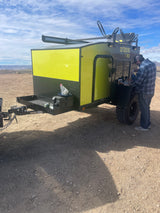 A man attends to a bright yellow Outbound T-Rex overland trailer. This RV rental is perfect for desert camping adventures.
