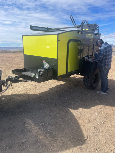 A man attends to a bright yellow Outbound T-Rex overland trailer. This RV rental is perfect for desert camping adventures.