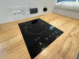 RV rental kitchen setup with a built-in induction cooktop, electrical outlets, and power control panel on a wood counter.