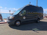 A black rv rental van (CLIFF logo) is parked by an ocean marina with boats & palm trees under a sunny sky.