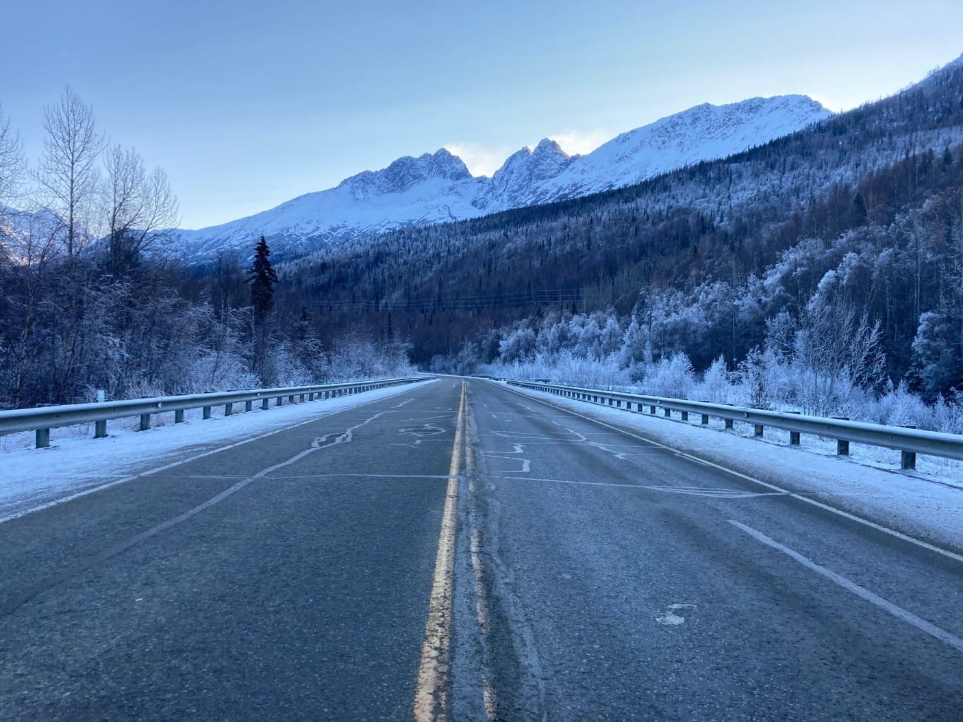 A snow-dusted road with guardrails leads to majestic mountains. Imagine your RV rental exploring this stunning winter scene!