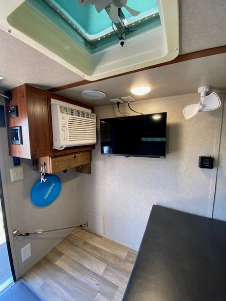 Inside a compact RV rental, featuring an AC unit, wall-mounted TV, ceiling fan, and bright skylight for comfort.