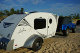A white Luna teardrop RV rental hitched to a blue Jeep, ready for beach or sand dune camping.