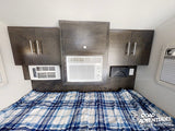 Cozy RV rental bedroom with a plaid bed, overhead cabinets, and dual AC units, perfect for comfortable road adventures.
