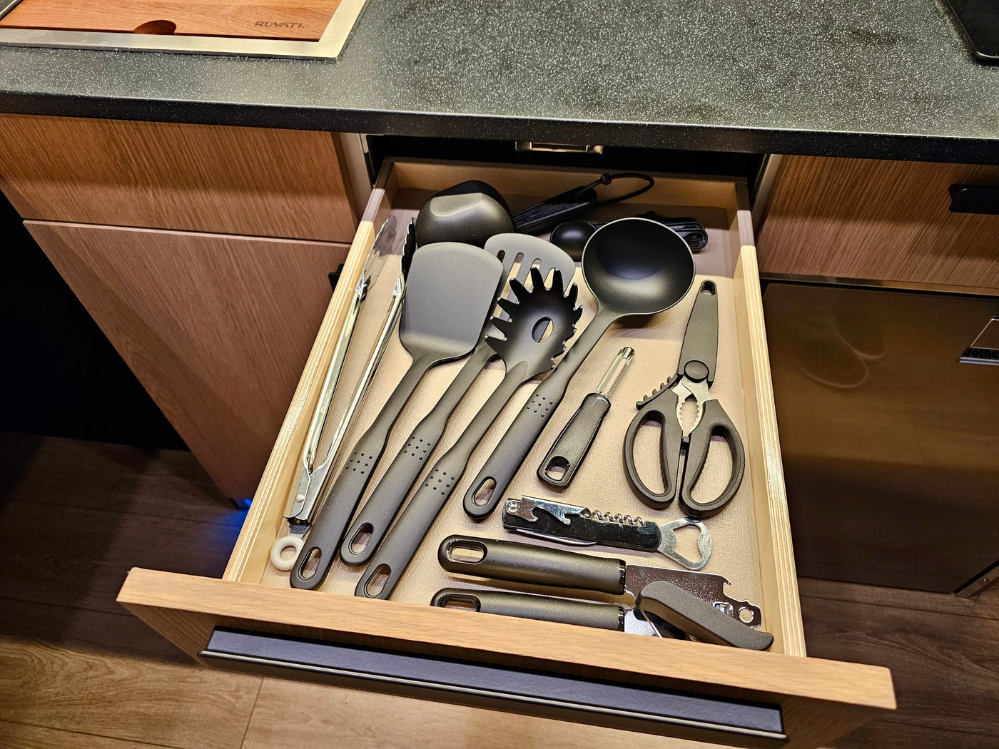 Black kitchen utensils neatly arranged in a wooden drawer, perfect for your RV rental cooking. — photo 11