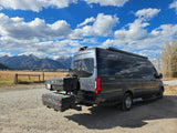 An RV rental van with rear storage, parked on a scenic dirt road, facing majestic mountains and a cloudy sky. Perfect for outdoor adventure.