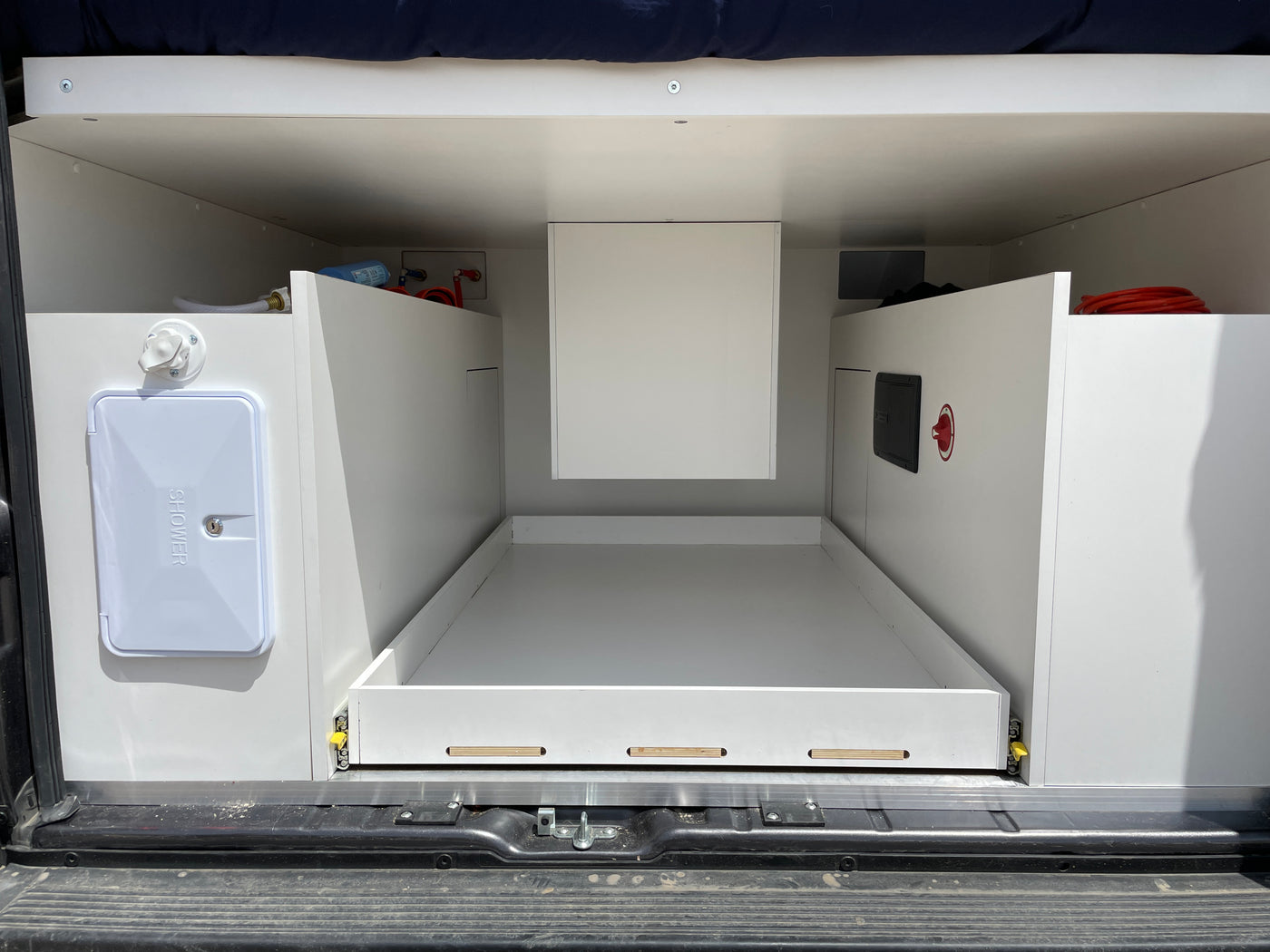 Inside an RV rental: rear utility area with pull-out storage, outdoor shower, and visible plumbing/electrical connections. — photo 10