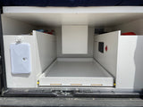Inside an RV rental: rear utility area with pull-out storage, outdoor shower, and visible plumbing/electrical connections.