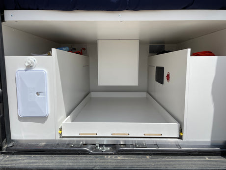Inside an RV rental: rear utility area with pull-out storage, outdoor shower, and visible plumbing/electrical connections.
